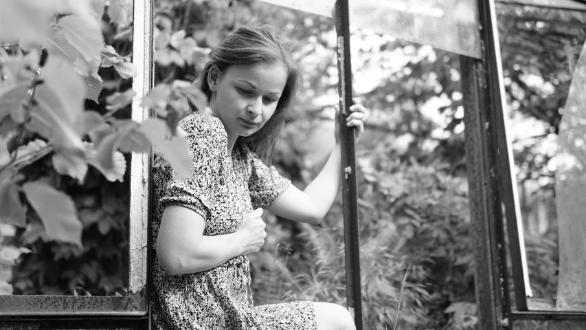 a black and white image of a girl sitting on a window sill
