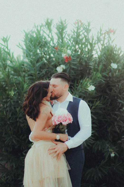 couple kissing in front of a bush with flowers