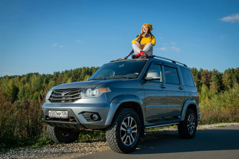 a woman with a yellow top is on top of a gray suv