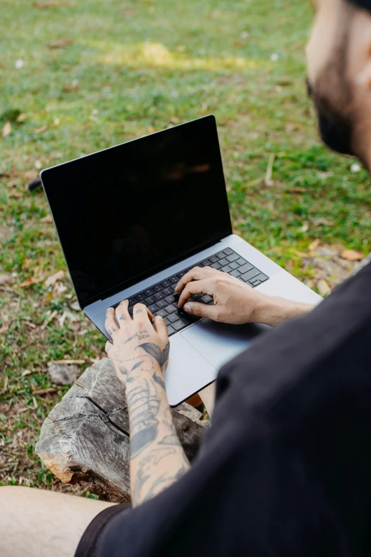 a man uses his laptop while sitting on the grass