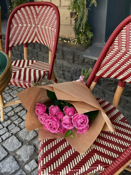 pink flowers wrapped in a brown paper on top of two chairs