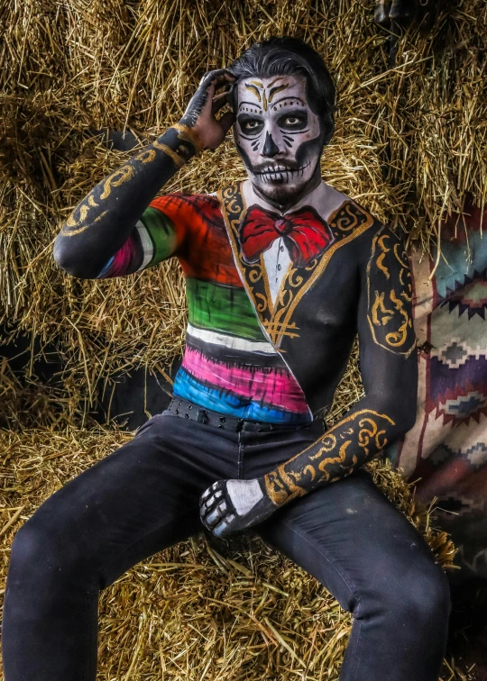 a woman with body paint is sitting next to a straw bale