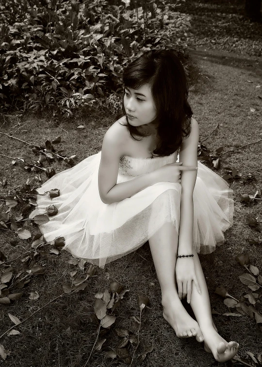 black and white po of young female in lace dress sitting on the ground