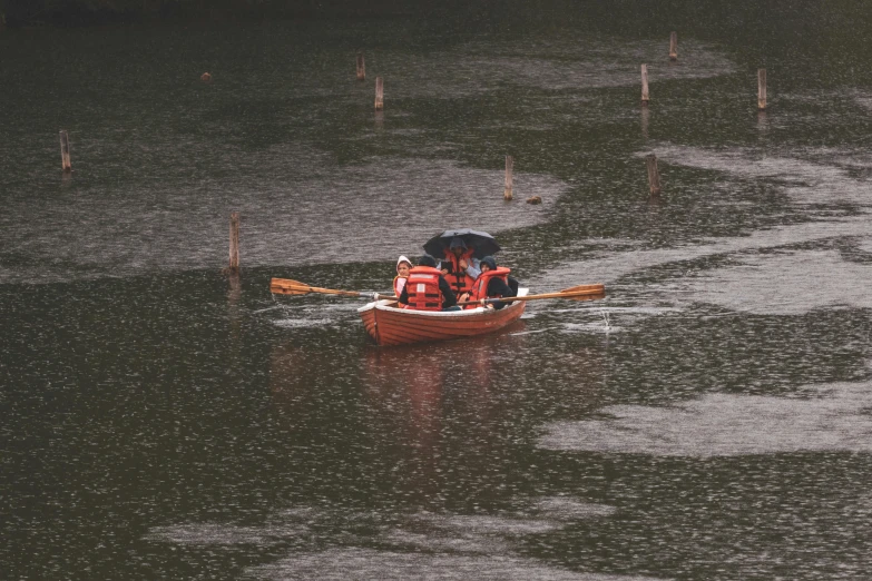 an oarboat on the water, with one person in it and two others