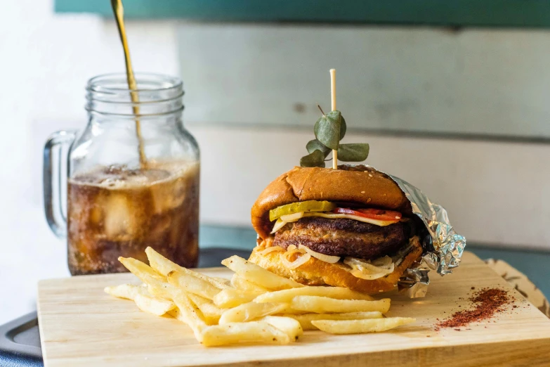 a hamburger and fries sit on a wooden board next to a beverage