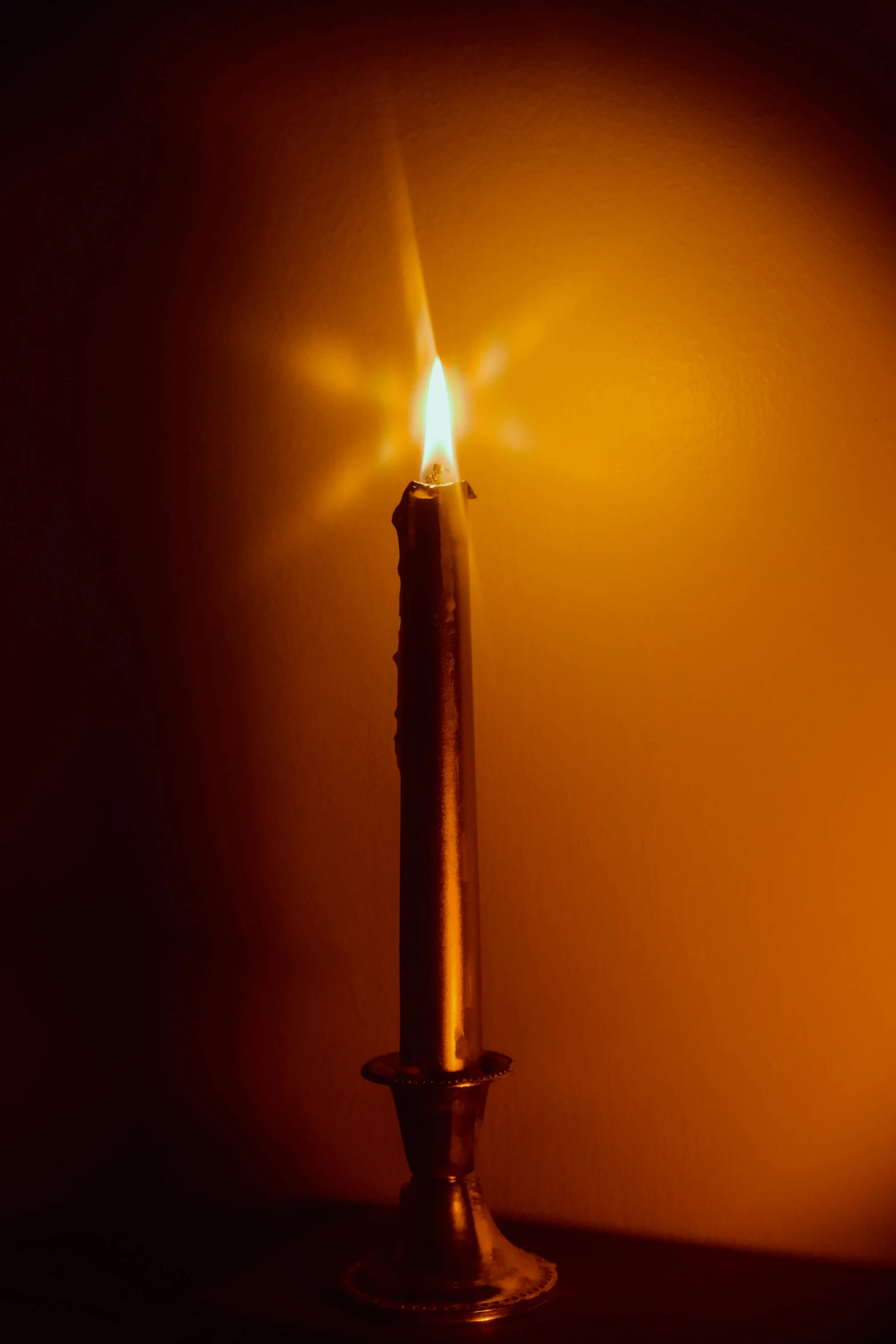 a tall candle on top of a table lit by a candlelight