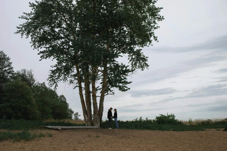 two people standing in the dirt by a large tree