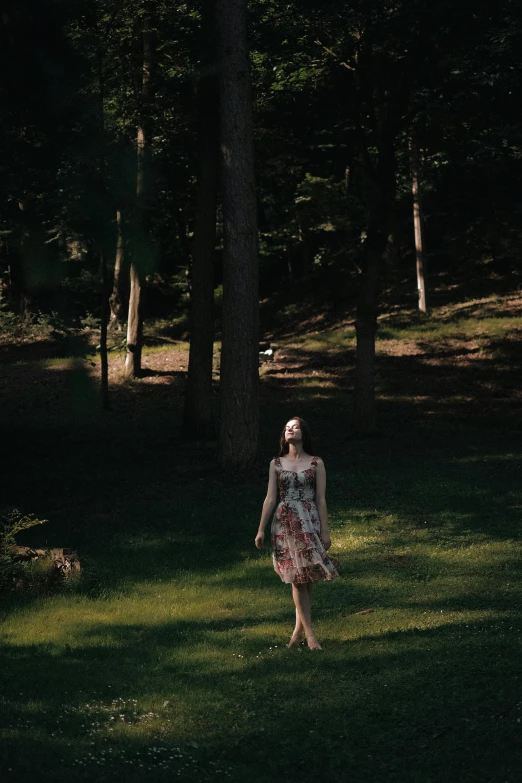 a woman in a dress stands by some trees