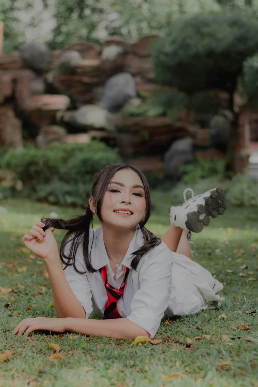 an asian girl in uniform lays on the grass while posing for her po