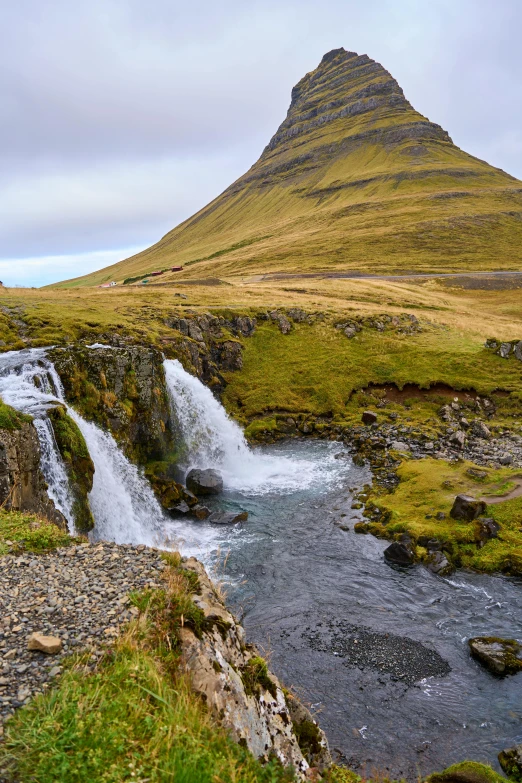 water flows down a small river in front of a grassy, mountainous hill