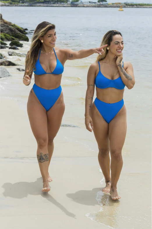 two women walking in the sand while wearing swimsuits