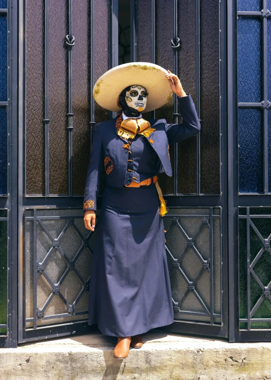 a mexican woman dressed in blue with a sombrero standing in front of a wrought iron gate