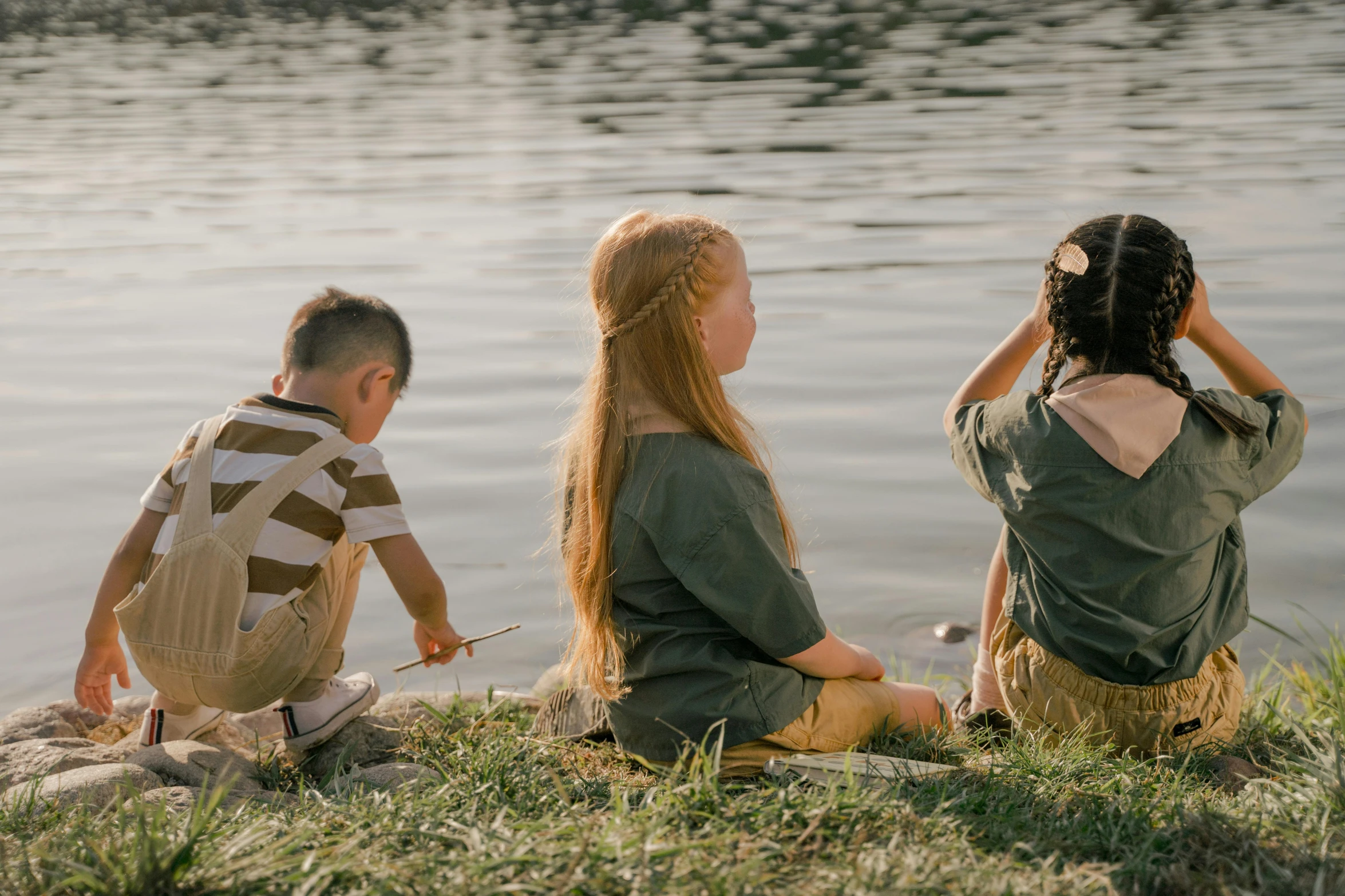 two girls and a man sitting near a lake