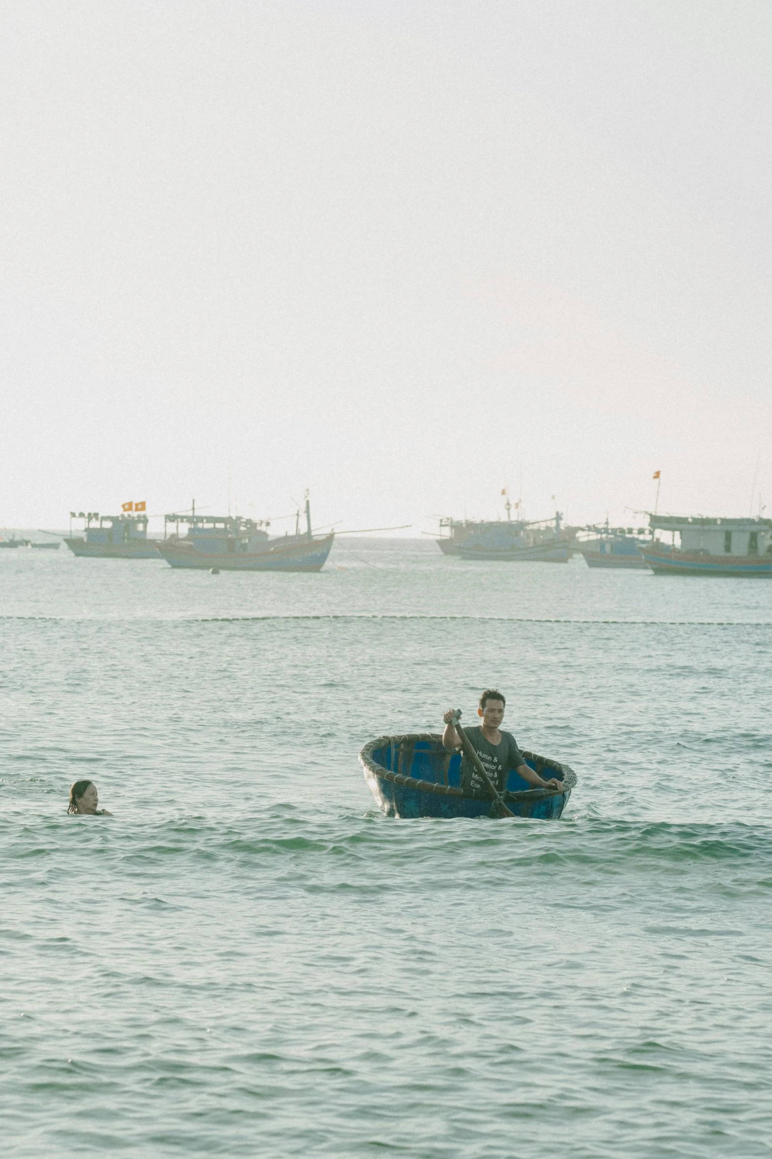 two people on a blue row boat with several ships in the background