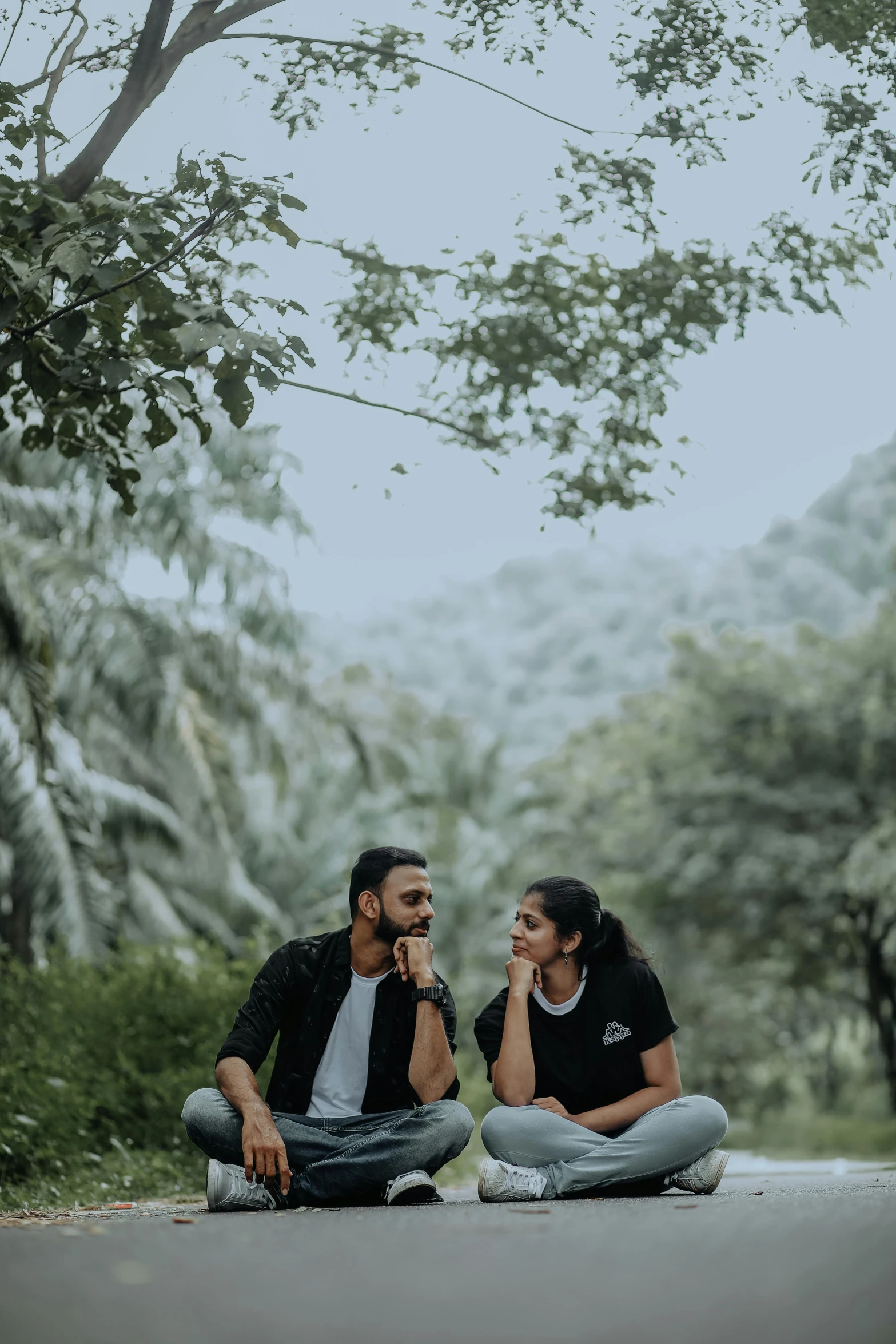 a couple sitting on the road, one holding his face to his mouth and looking at the other