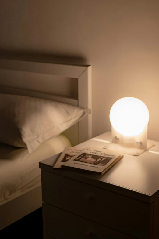 a small bedside table with magazine, book and lights in a small room