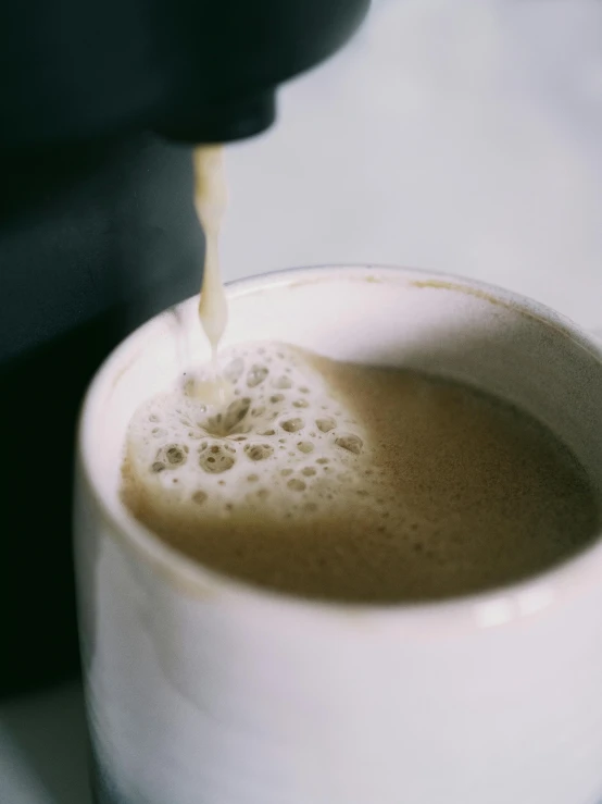 a white coffee mug filled with liquid being poured into it