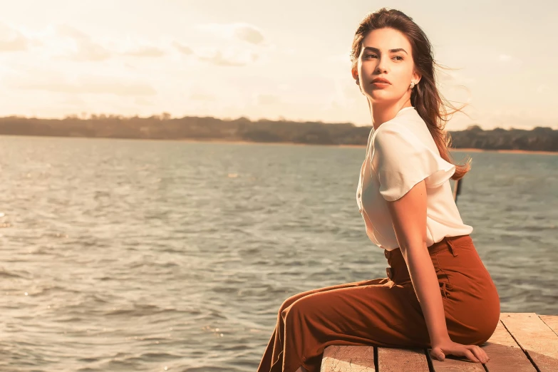 a woman is sitting on the dock by the water