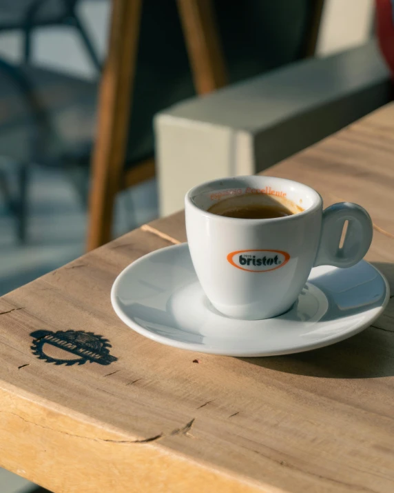 a cup of coffee on a wooden table with chairs in the background