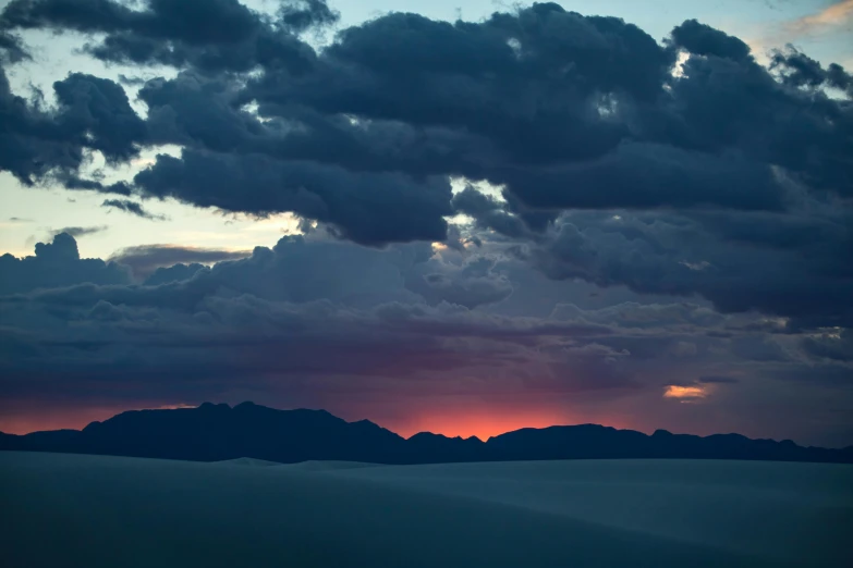 the sun setting behind mountains on an overcast day