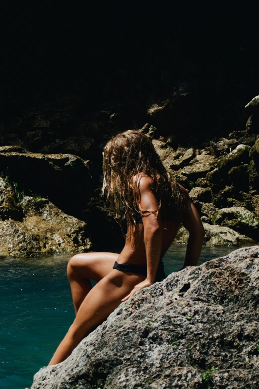 a beautiful young woman wearing a bikini sitting on top of a large rock