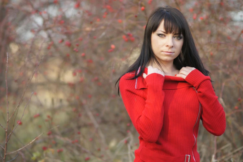 a woman with long black hair and eyes wearing a red top is standing in front of trees