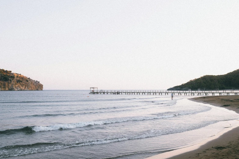 a beach with the ocean waves and bridge on it