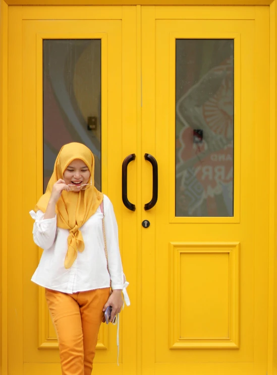 a woman standing by a yellow door smiling