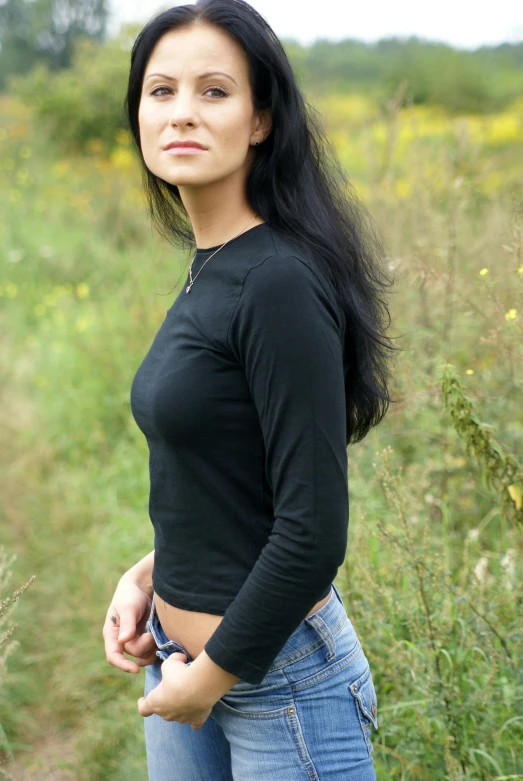 a girl in jeans and black top standing in the grass