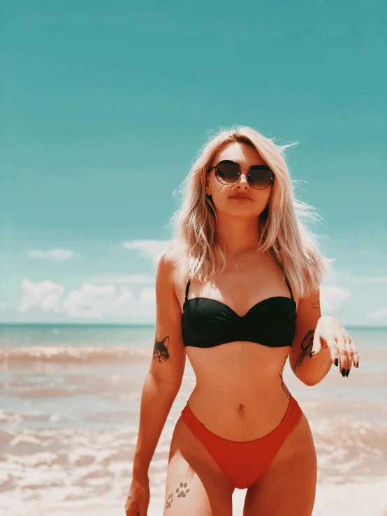 a woman in a bikini and sunglasses on a beach