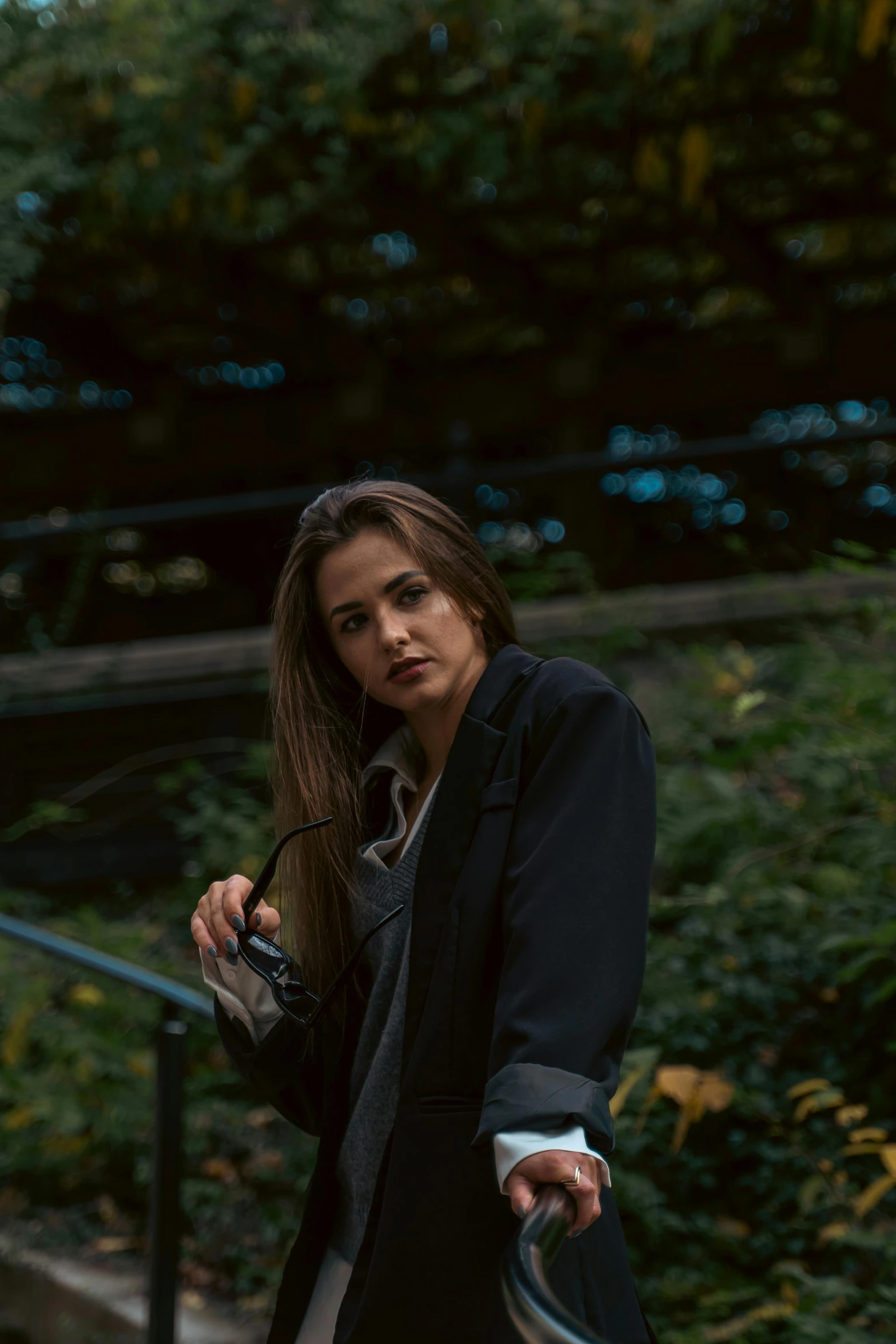 woman in black coat with camera and glasses posing by steps