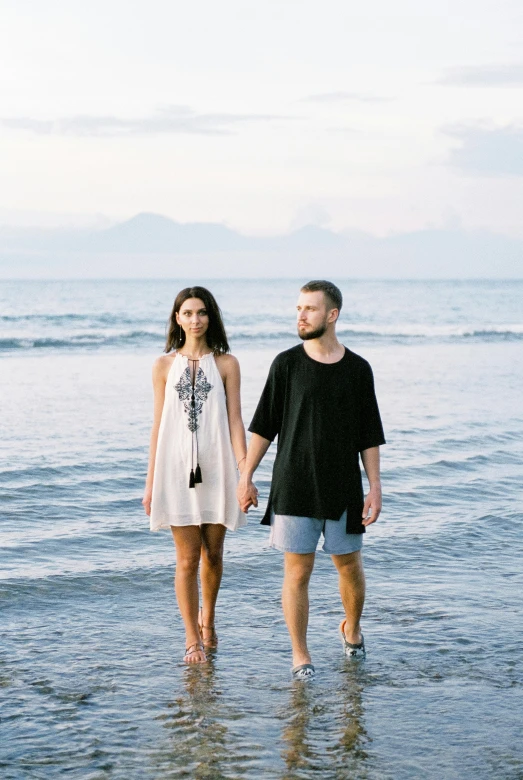 a young couple holds hands as they stand on a beach