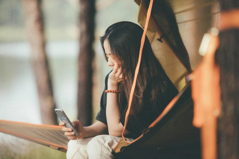 woman sitting in a hammock looking at a cell phone