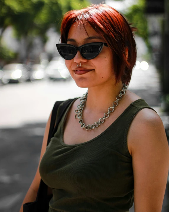 a red headed woman wearing black sunglasses, carrying a purse and looking at the camera