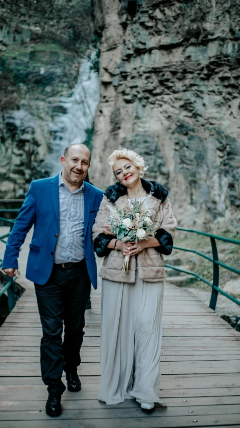 a man and woman walking on a bridge by a waterfall