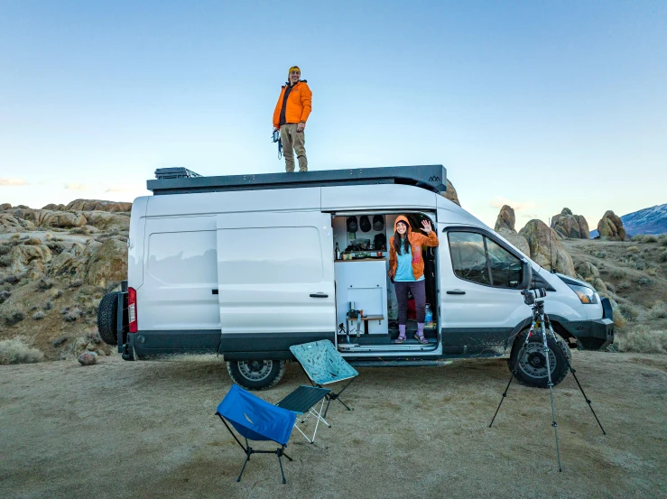 two people stand on the roof of a van