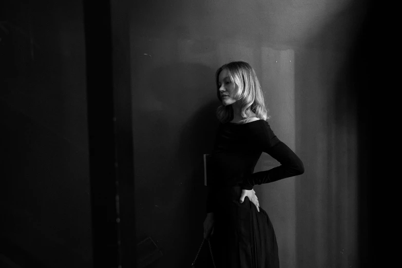 a young woman poses in front of a wall in a dark room