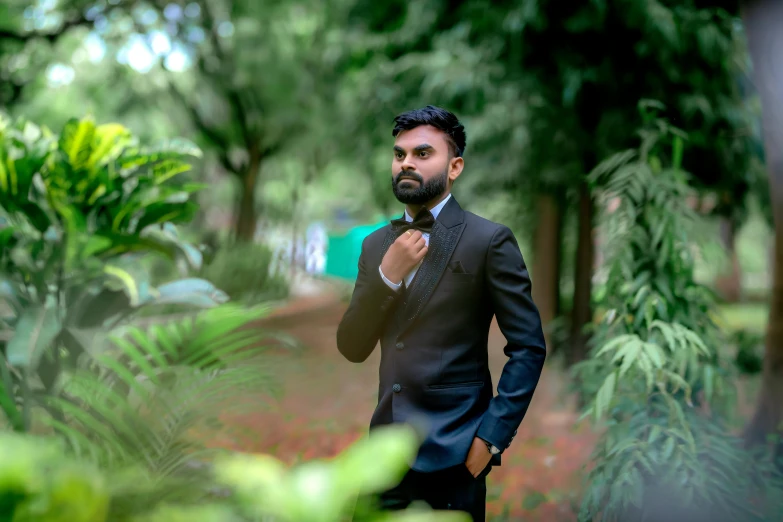 a man in a tuxedo standing under trees