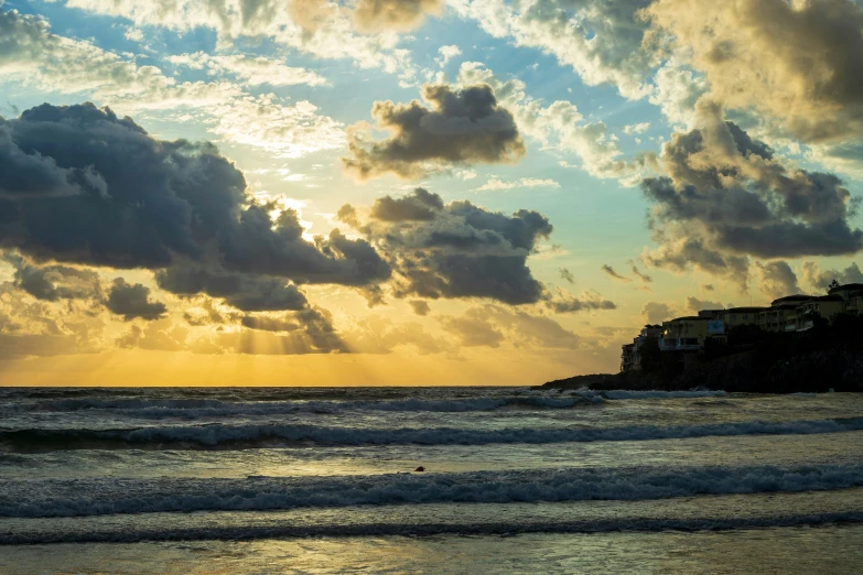 the sun shines down behind clouds and houses on a beach