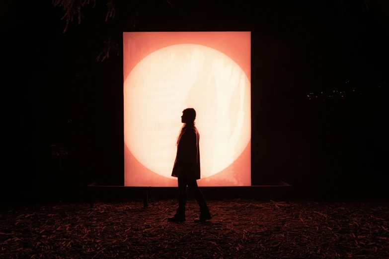 a woman looks at an orange light displayed in a dark field