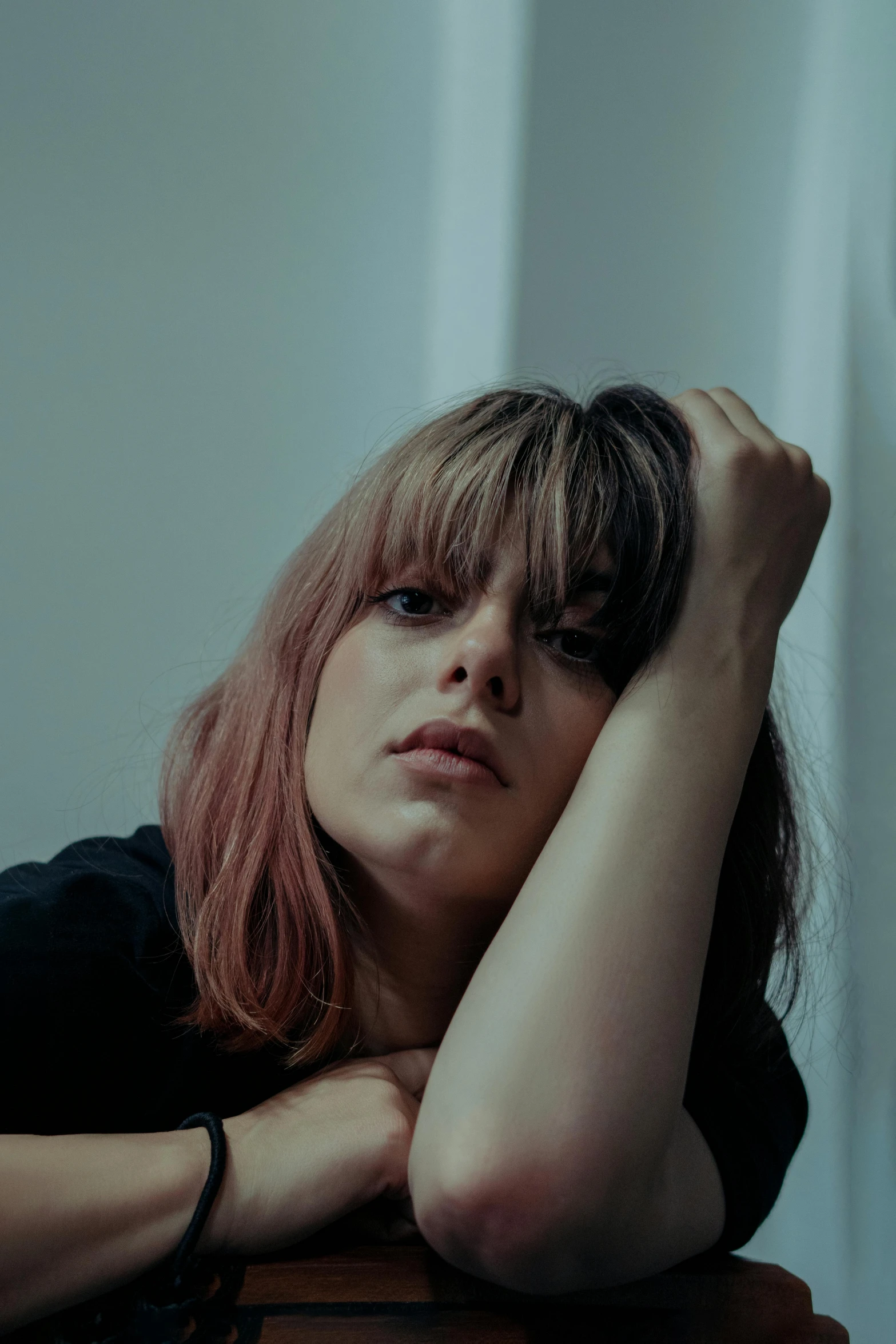 a beautiful woman sitting next to a wooden table with her hand resting her head