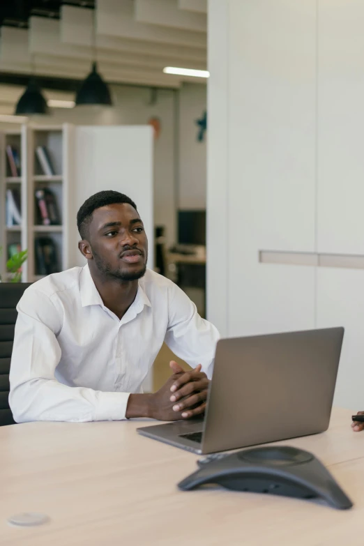 a man in white shirt sitting at a desk using a laptop