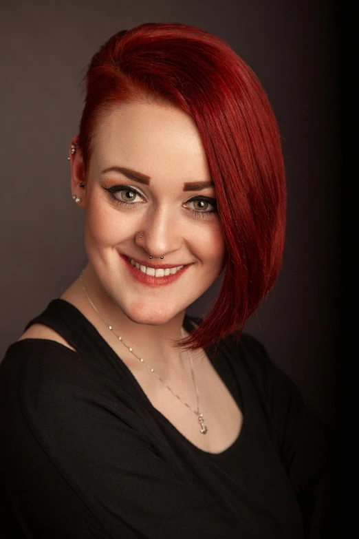 a woman with bright red hair and piercings smiles