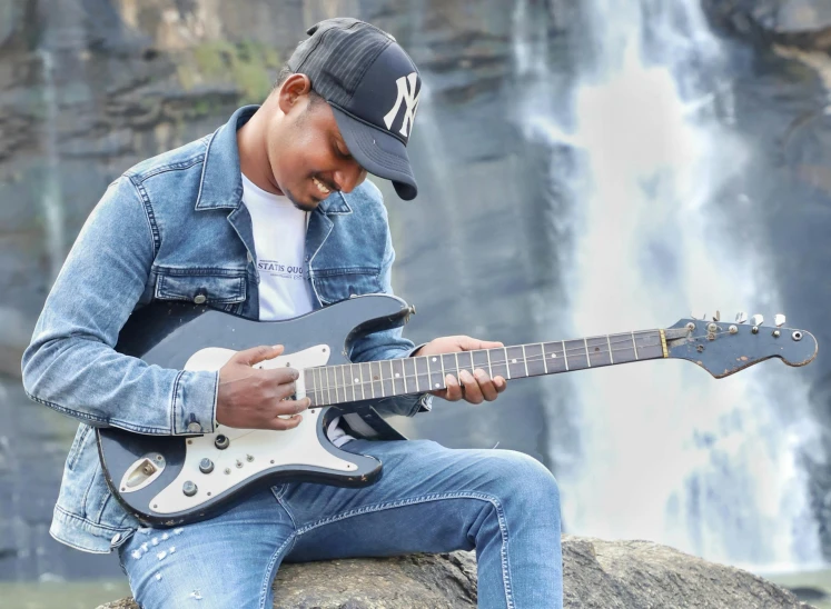 a person playing guitar sitting on the rock by the waterfall