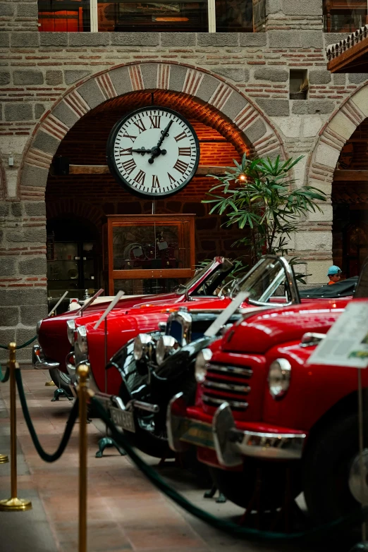 a row of red vintage cars parked underneath a clock