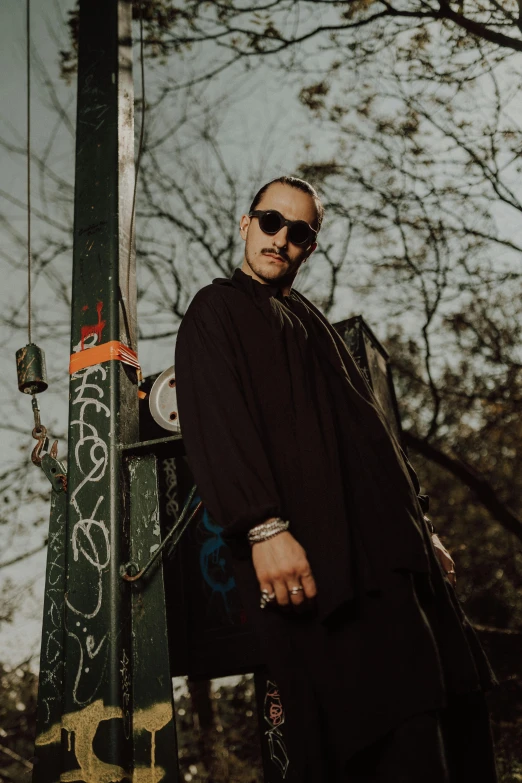 man with sunglasses standing next to a graffiti - covered pole