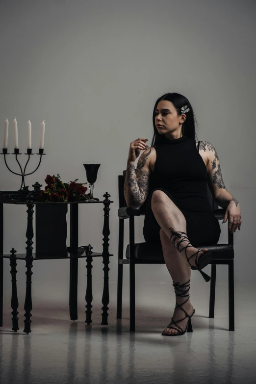a girl with black tattoo on sitting in a chair next to a table