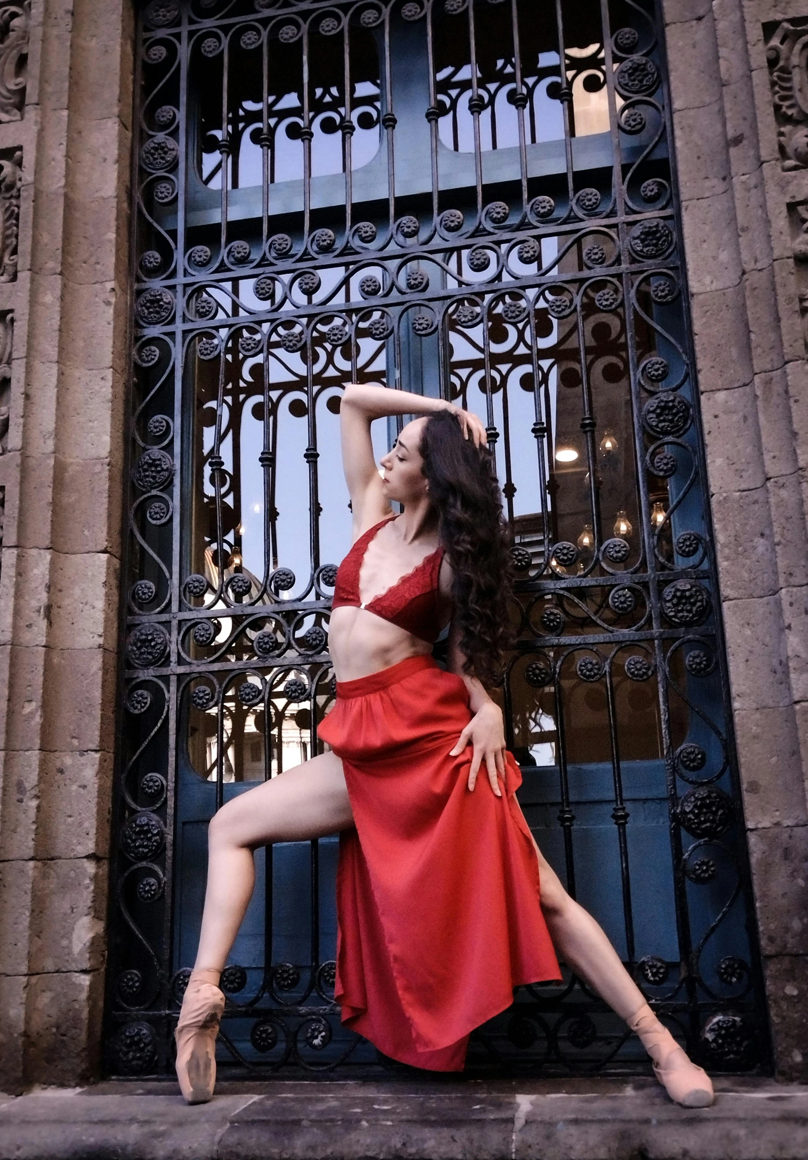 a woman in a red dress and high heels posing by an iron gate