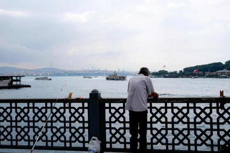 the man watches boats in the ocean from behind a fence