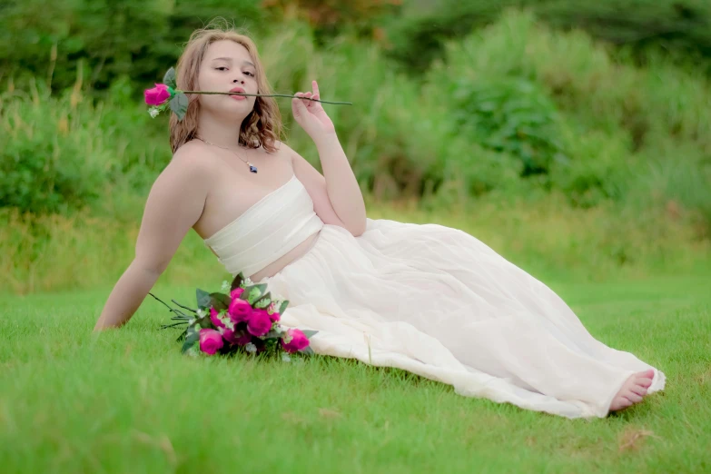 young woman in wedding dress with pink flowers on her head sitting in grassy field